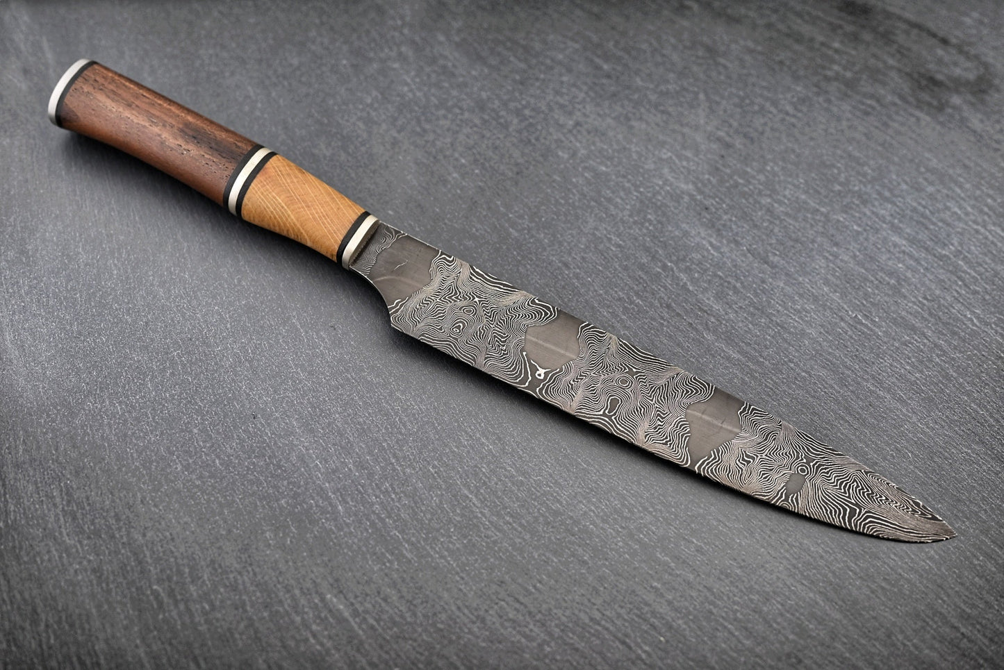 Liegendes Damastmesser: schmale Klinge mit Holzgriff und ausgeprägtem Damastmuster
