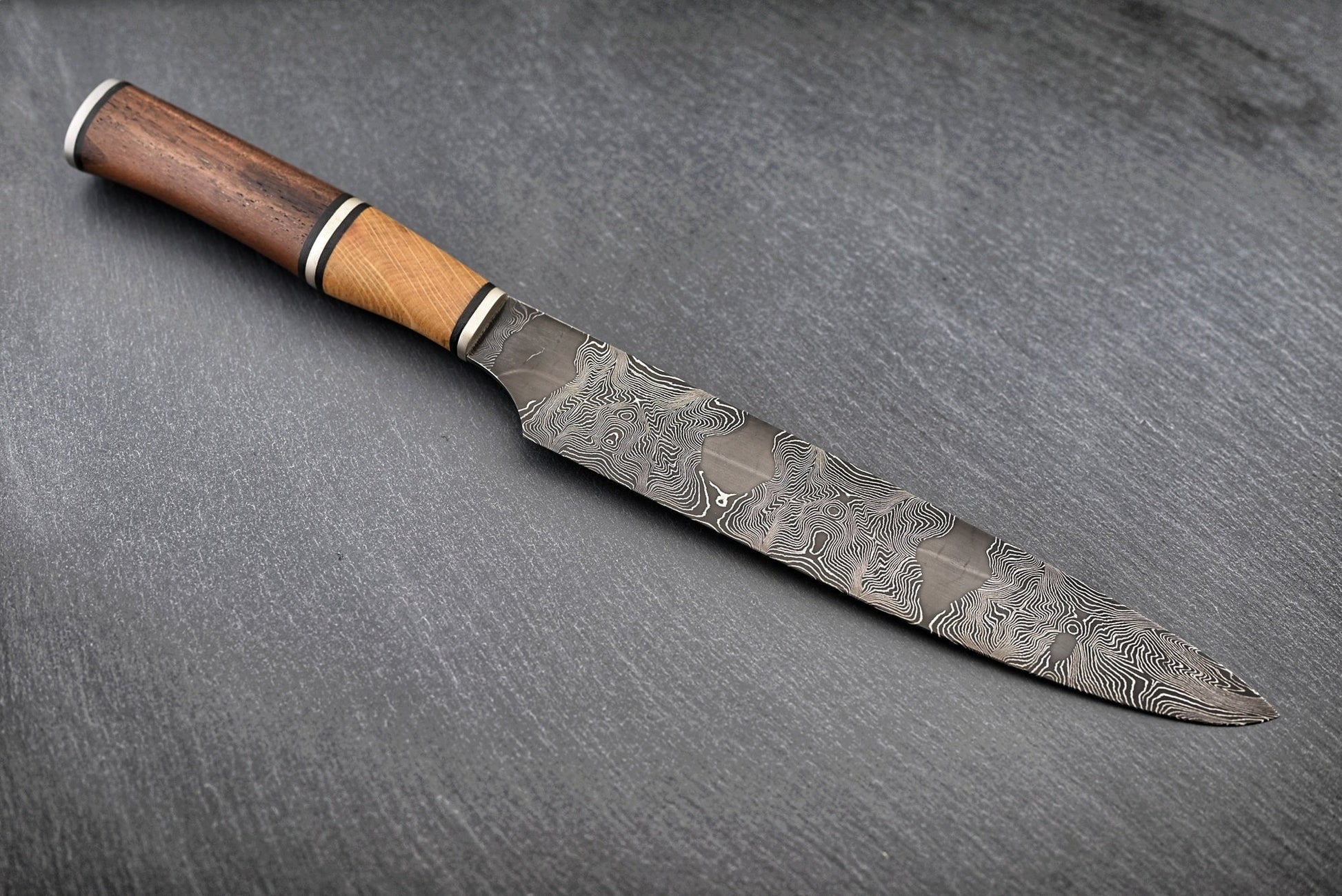 Liegendes Damastmesser: schmale Klinge mit Holzgriff und ausgeprägtem Damastmuster