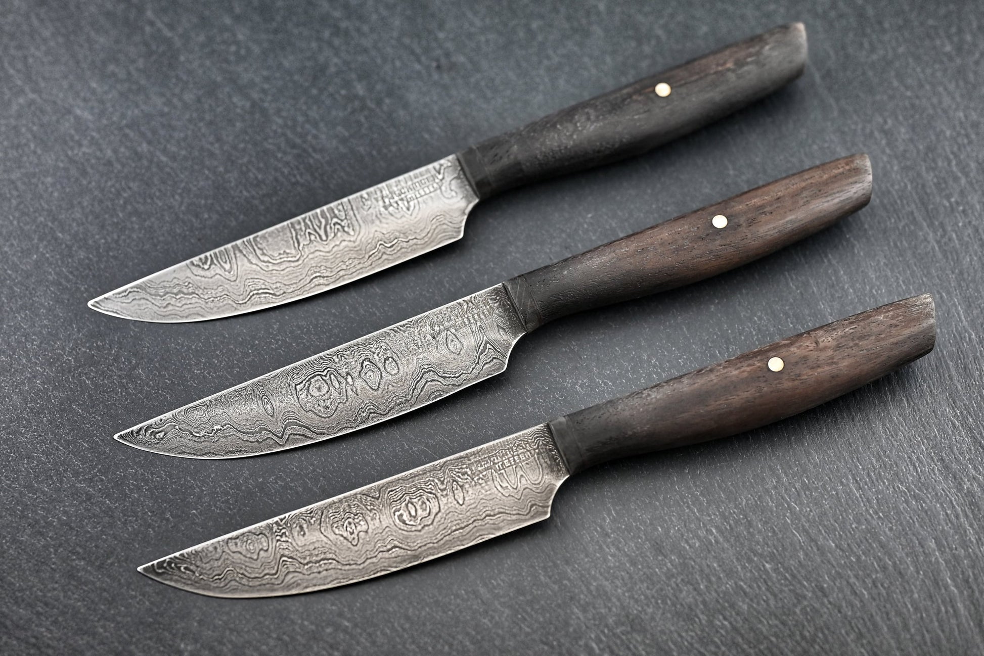3 Damast-Steakmesser mit Holzgriffen und sichtbarem Damaskus-Muster auf den Klingen