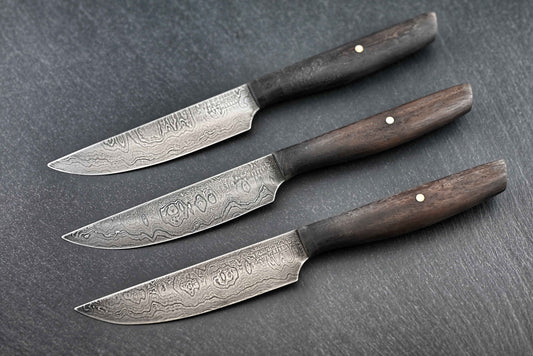 3 Damast-Steakmesser mit Holzgriffen und sichtbarem Damaskus-Muster auf den Klingen